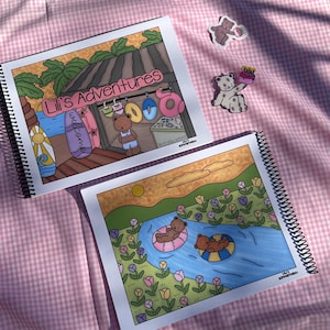 May include: Two spiral-bound notebooks with colorful illustrations of bears at the beach and in a river. The top notebook reads "Lili's Adventures" and features a bear at a beach stand. Two bear stickers are also visible.