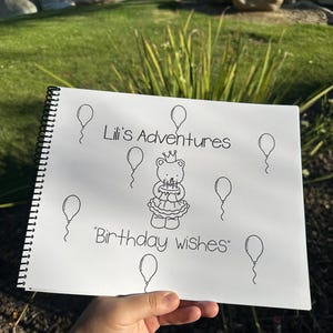 May include: A spiral-bound notebook with the text "Lili's Adventures" and "Birthday wishes" in black ink. The notebook features a drawing of a bear wearing a crown and holding a cake, surrounded by balloons.