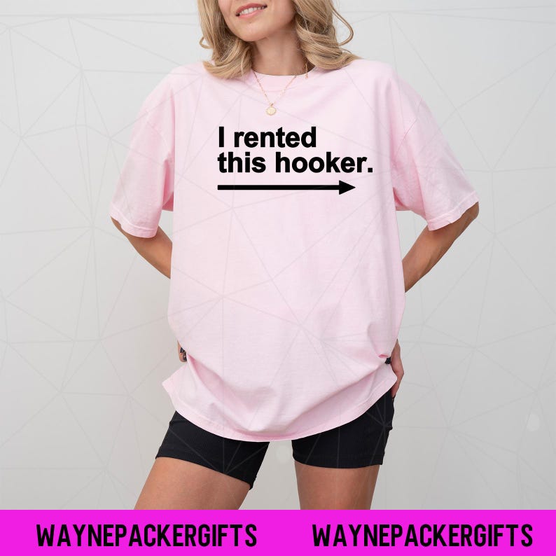 Puede incluir: Camiseta rosa claro con el texto negro "I rented this hooker" y una flecha hacia la derecha. La camiseta se combina con pantalones cortos negros. La parte inferior de la imagen muestra "WAYNEPACKERGIFTS" en blanco sobre un fondo rosa.