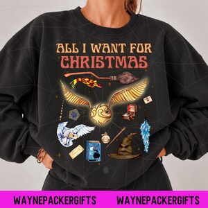 May include: A black crewneck sweatshirt featuring the text ALL I WANT FOR CHRISTMAS in orange letters. The graphic includes a golden snitch, a broomstick, a striped scarf, a white owl, a sorting hat, a blue book, a potion bottle, and a wand.