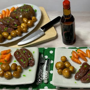 May include: Three plates of food with roasted vegetables, potatoes, and meat. Each plate is set with a fork and knife. A bottle of wine and two glasses of red wine are also on the table.