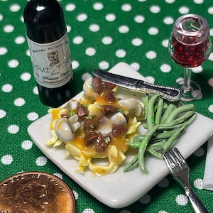 Könnte beinhalten: Ein weißer Miniaturteller mit einer Portion Pasta, Pilzen und Soße, dazu grüne Bohnen, ein Miniaturmesser und eine Gabel. Auf dem Bild sind auch eine Miniaturflasche Rotwein und ein Glas Rotwein zu sehen.