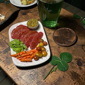 May include: A white ceramic mug with a black handle and the text "But First, Coffee" in a bold, black font. The mug is set against a blurred background, suggesting a cozy setting.