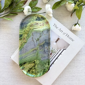 May include: An oval-shaped tray featuring a marbled pattern in shades of lime green, forest green, and slate gray. The surface has a smooth, polished finish with natural-looking veining throughout, creating a distinct, organic appearance.
