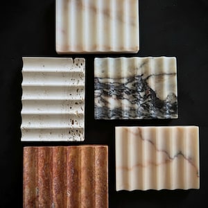 Puede incluir: Cinco jaboneras diferentes hechas de varios tipos de mármol. Las jaboneras son todas rectangulares y tienen un diseño ondulado. El mármol es en tonos de blanco, beige, marrón y gris.