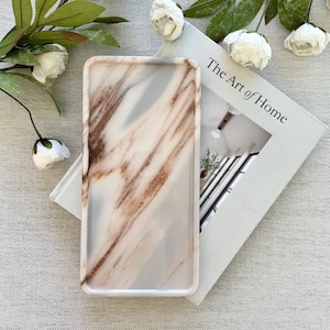 May include: A rectangular tray with a smooth, polished surface featuring a marbled pattern of white, grey, and copper-brown veins. The tray has slightly raised edges and a glossy finish, showcasing a natural stone-like appearance in its design.