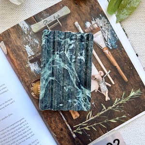 May include: A rectangular soap dish made of dark green marble with white veining. The dish has a ridged surface and is displayed on a magazine. The number "202" is visible in the bottom right corner.