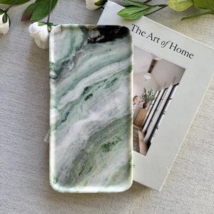 May include: A rectangular tray made of polished stone featuring a marbled pattern with swirling shades of forest green, sage, and white. The tray has smooth, rounded edges and a glossy finish, displaying natural veining throughout the surface.