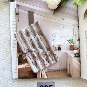 May include: A rectangular, corrugated decorative piece with a weathered, textured appearance. The piece features shades of brown, gray, and white, resembling aged metal. The number "205" is visible on a gray label. The piece is resting on an open magazine.