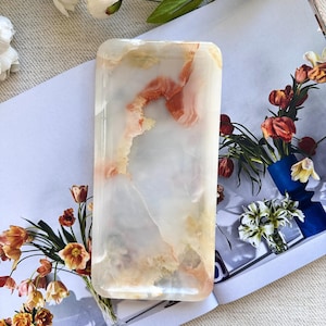May include: A rectangular tray crafted from polished stone, featuring a translucent white base with swirling veins of soft orange and peach. The surface is smooth and glossy, showcasing natural mineral patterns throughout the entire piece.