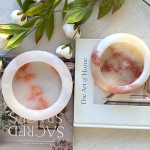 May include: A white ceramic mug with a black handle and the text "But First, Coffee" in a bold, black font. The mug is on a wooden surface. The mug is approximately 10 cm tall.