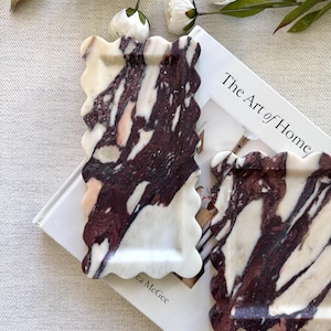 May include: Two rectangular trays with scalloped edges, crafted from polished stone featuring a marbled pattern of deep burgundy and creamy white veins. The trays have a smooth, glossy finish and a distinct wavy border design along all four sides.