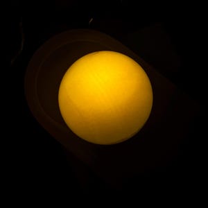 May include: A glowing yellow sphere, possibly a light source, is centered in a dark environment. The sphere has a soft, diffused glow, suggesting it might be a lamp or a decorative element. The background is a deep black.