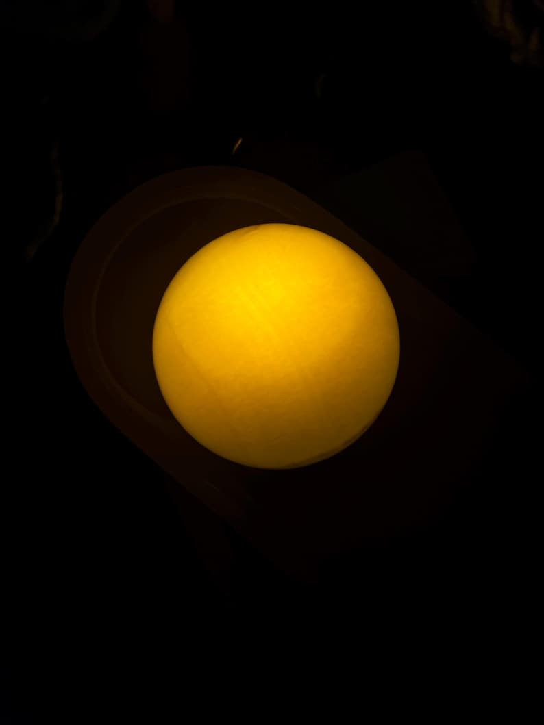 May include: A glowing yellow sphere, possibly a light source, is centered in a dark environment. The sphere has a soft, diffused glow, suggesting it might be a lamp or a decorative element. The background is a deep black.