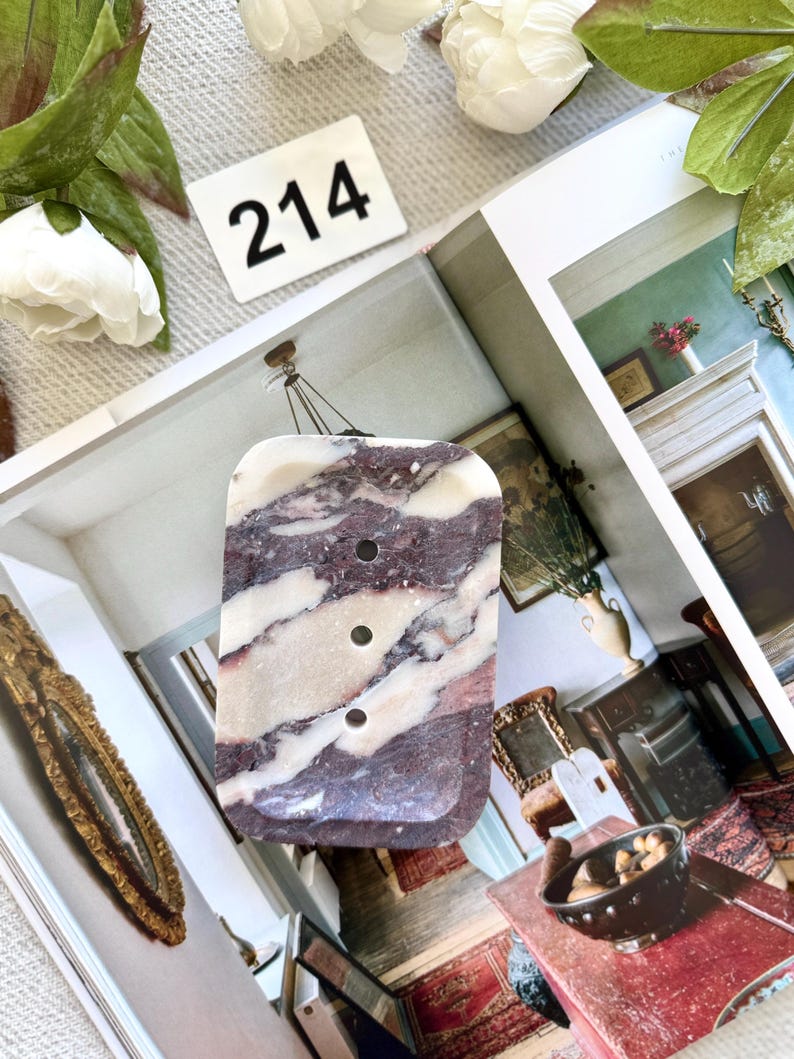 May include: A rectangular pendant with a marbled pattern of burgundy and white. The pendant has three circular holes and is suspended by a thin cord. A white tag with the number "214" is visible in the background.
