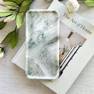 May include: A rectangular tray with a polished surface featuring a white and sage green marbled pattern. The tray has rounded corners and a smooth, glossy finish, showcasing natural-looking veining throughout the stone-like material.