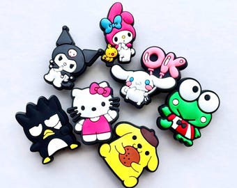 May include: A collection of colorful cartoon character charms, including a black penguin, a yellow dog with a cookie, and a green frog. Other characters include a white bunny, a pink cat, and a black bat. The charms are made of a rubbery material.