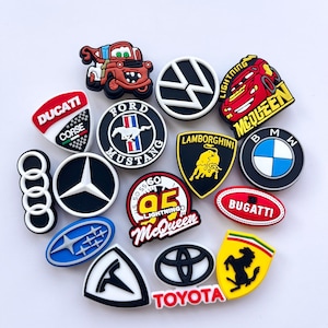 Op de afbeelding: Een verzameling kleurrijke schoenbedels met diverse automerkenlogo's en karakterontwerpen, waaronder Ducati, Ford Mustang, Volkswagen, Lamborghini, BMW, Audi, Mercedes-Benz, Lightning McQueen, Bugatti, Subaru, Tesla, Toyota en Ferrari.