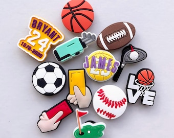 May include: A collection of sports-themed charms, including a basketball, football, soccer ball, and baseball. Other charms feature a golf bag, tennis racket, and a basketball hoop with the word "LOVE". There are also charms with the names "BRYANT 24" and "JAMES 23".