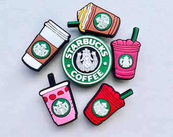 May include: A collection of colorful Starbucks-themed charms. The charms include coffee cups, Frappuccinos, and a circular logo with the Starbucks name and logo. The charms are in shades of brown, pink, and red, with green and white accents.