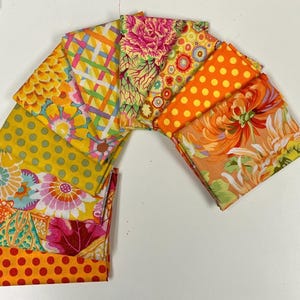 May include: A collection of folded fabric squares arranged in a fan shape, featuring various patterns including orange polka dots, yellow circles, floral prints, and lattice designs in vibrant shades of orange, yellow, pink, and green.