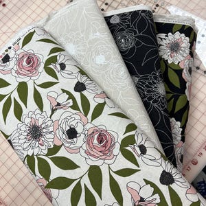 Peut inclure: Quatre rouleaux de tissu floral de différentes couleurs. L'un présente un fond blanc avec des fleurs roses et blanches et des feuilles vertes. Un autre a un fond beige avec des contours floraux blancs. Le troisième est noir avec des contours floraux blancs, et le quatrième est noir avec des fleurs roses et blanches.