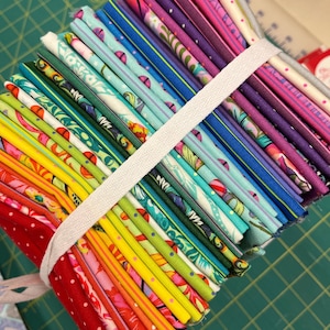 May include: A stack of colorful fabric squares, tied together with a white ribbon. The fabrics feature various patterns, including floral, geometric, and polka dots.