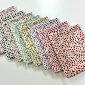 Peut inclure: Plusieurs morceaux de tissu pliés, chacun orné d'un motif floral distinct. Les motifs présentent de petites fleurs stylisées dans diverses couleurs, notamment le violet, le bleu, le vert et le rouge, sur fond crème.