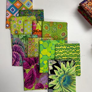 May include: A collection of folded fabric squares in various vibrant patterns and colors. The fabrics feature designs including geometric shapes, floral prints, and botanical illustrations. The color palette includes shades of green, pink, purple, and orange.