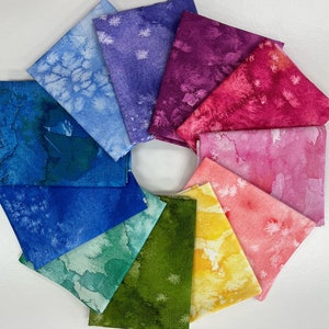 May include: A set of ten fabric squares in various shades of blue, green, yellow, orange, pink, and purple. Each square has a watercolour-like design with white speckles.