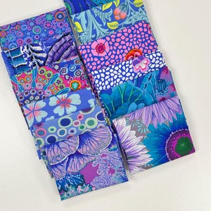 Pode incluir: Uma coleção de quadrados de tecido dobrados dispostos em duas colunas, apresentando padrões vibrantes em tons de azul, roxo, rosa e verde. Os designs incluem motivos florais, círculos abstratos, formas orgânicas e estampas botânicas complexas.