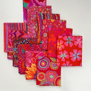 Pode incluir: Uma pilha de 10 quadrados de tecido vermelho com vários padrões coloridos, incluindo círculos, listras, flores e designs abstratos.