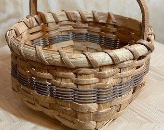 Cesta tejida a mano con tiras, firmada por el artista en 1986. Cesta pequeña de estilo rústico con asa de madera. Ideal para decoración rústica y almacenamiento.