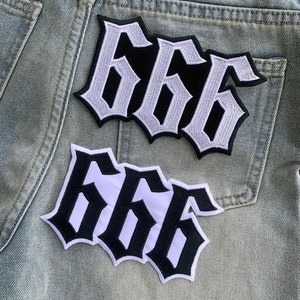 Puede incluir: Dos parches bordados con el número "666" en una fuente gótica. Los parches son negros con costuras blancas, sobre un fondo de mezclilla azul claro. Estos parches son probablemente para ropa.