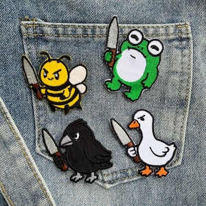 May include: Four embroidered patches featuring a yellow bee, a green frog, a black crow, and a white goose, each holding a small silver knife with a brown handle. The patches are arranged on the back pocket of a pair of blue denim jeans.