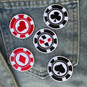 May include: Five embroidered poker chip patches in red, white, and black, featuring hearts, diamonds, clubs, and spades. The patches are arranged on a denim pocket, showcasing a casino or gambling theme.
