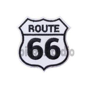 Puede incluir: Parche bordado blanco y negro con el texto "ROUTE 66" dentro de una forma de escudo.