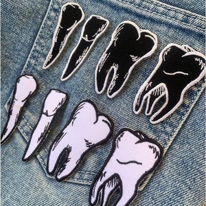 May include: A collection of embroidered iron-on patches featuring teeth in various styles. Some patches are white with black outlines, while others are black with white outlines.