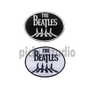 Op de afbeelding: Twee geborduurde patches met het Beatles-logo. De bovenste patch is zwart met witte letters en de onderste patch is wit met zwarte letters. Beide patches tonen de iconische Beatles 'Abbey Road' oversteek afbeelding.