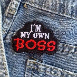 Op de afbeelding: Een geborduurde zwarte en rode patch met de tekst "I'm My Own Boss" in witte letters. De patch heeft de vorm van een wolk en is genaaid op een blauwe denim achtergrond.