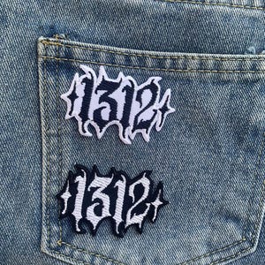 Puede incluir: Dos parches bordados en blanco y negro con el número "1312" en una fuente gótica, cosidos en un bolsillo de mezclilla azul.