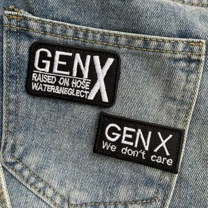 May include: Close-up of a light blue denim jeans pocket with two black embroidered patches. The patches read "GENX" with the phrases "RAISED ON HOSE WATER&NEGLECT" and "We don't care" in white lettering.