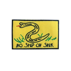 Può includere: Una toppa ricamata gialla con un serpente nero ed erba verde. Il testo "NO STEP ON SNEK" è scritto in nero sotto il serpente.