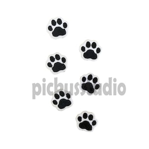 Könnte beinhalten: Fünf schwarze und weiße Bügelbilder in Form von Pfotenabdrücken. Die Pfoten sind weiß umrandet und haben eine schwarze Mitte.