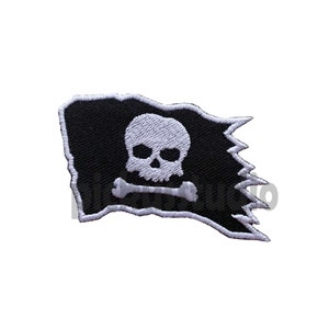 Puede incluir: Una bandera pirata negra con una calavera blanca y huesos cruzados bordados. La bandera está desgarrada y deshilachada en los bordes.