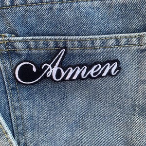 May include: A black and white embroidered patch with the word "Amen" in white lettering on a denim background.