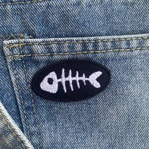 Könnte beinhalten: Ein schwarzer und weißer Fischgräten-Patch auf einem blauen Jeans-Hintergrund.
