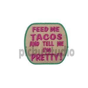Op de afbeelding: Beige geborduurde patch met groene rand. De tekst "Feed me tacos and tell me I'm pretty!" is geborduurd in roze draad.