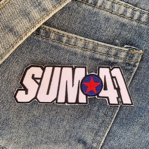Könnte beinhalten: Ein weißer und rosa gestickter Patch mit dem Text "SUM 41" in schwarzen Buchstaben und einem roten Stern in einem blauen Kreis.