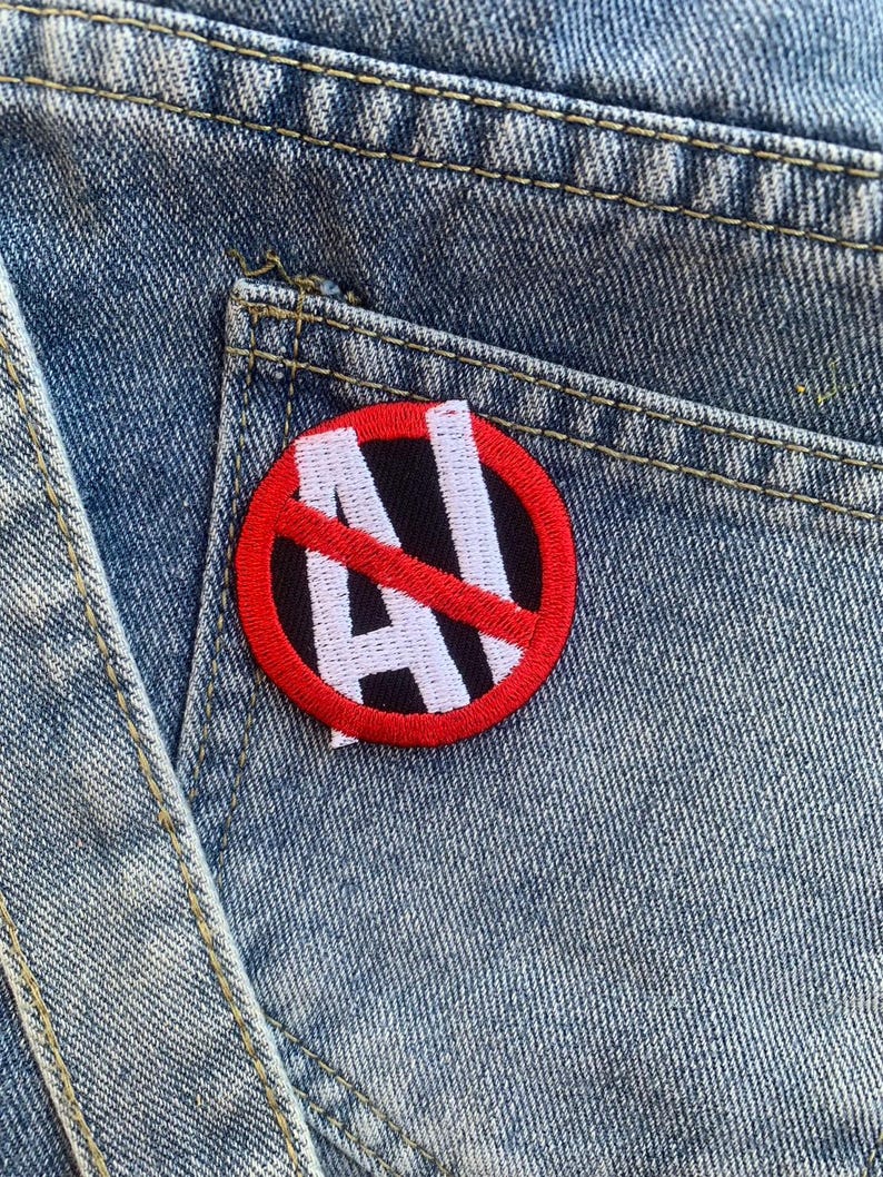 Puede incluir: Un c&iacute;rculo rojo con una l&iacute;nea diagonal que lo atraviesa, con las letras "AI" en blanco en su interior. El parche est&aacute; cosido en un bolsillo de mezclilla azul.